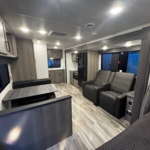 Modern RV interior with kitchen and reclining chairs.