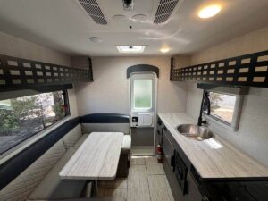 Compact camper interior with kitchenette and seating.