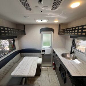 Compact camper interior with kitchenette and seating.
